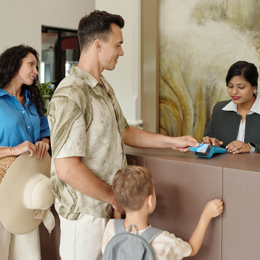 A family at a hotel front desk as a person pays by tapping a card on a payment terminal.