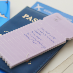 A purple notepad listing travel essentials like passport and visa, resting on top of a dark blue passport.