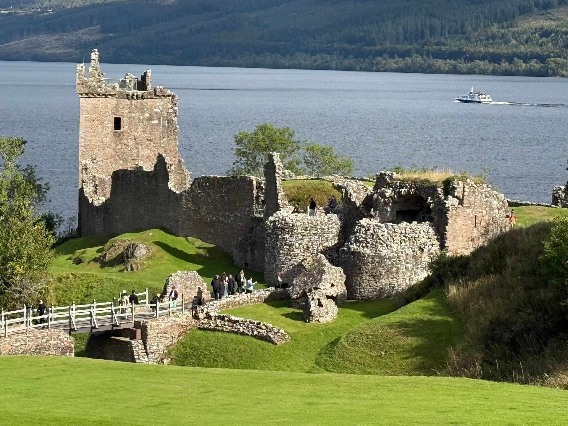 Ruins of Urquhart Castle on the shores of Loch Ness, Scotland, with a tour boat passing on the water.