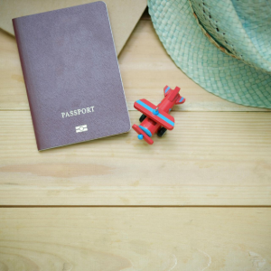 A purple passport, a small red toy airplane, and a light green sun hat arranged on a light wooden surface.