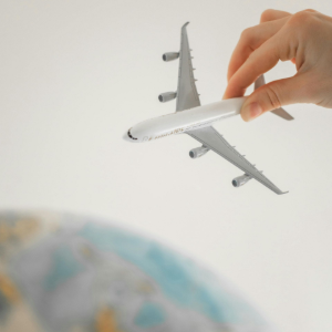 A hand holds a small toy airplane model positioned as if flying above a globe.