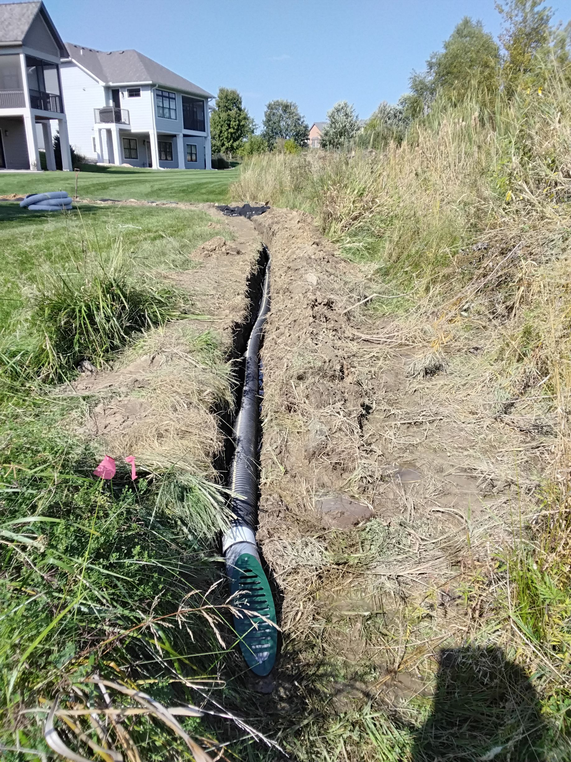 Our crew installing a 4 inch underground drain pipe leading from a French drain to outlet the water from French drain into a low area at far back end of backyard in naturalized space 