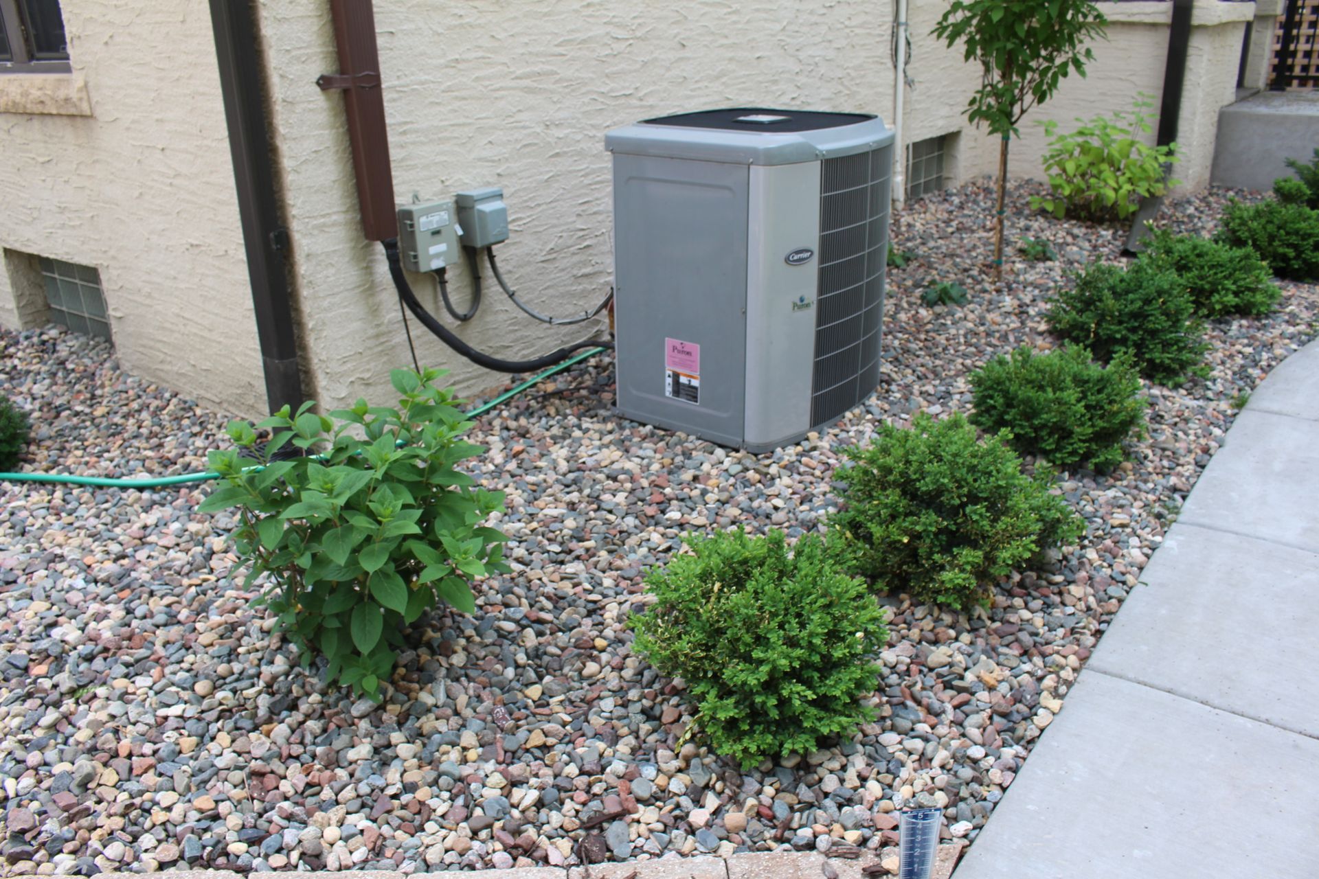 After photo of landscaping around house foundation with rock and plants screening the AC unit in Minneapolis