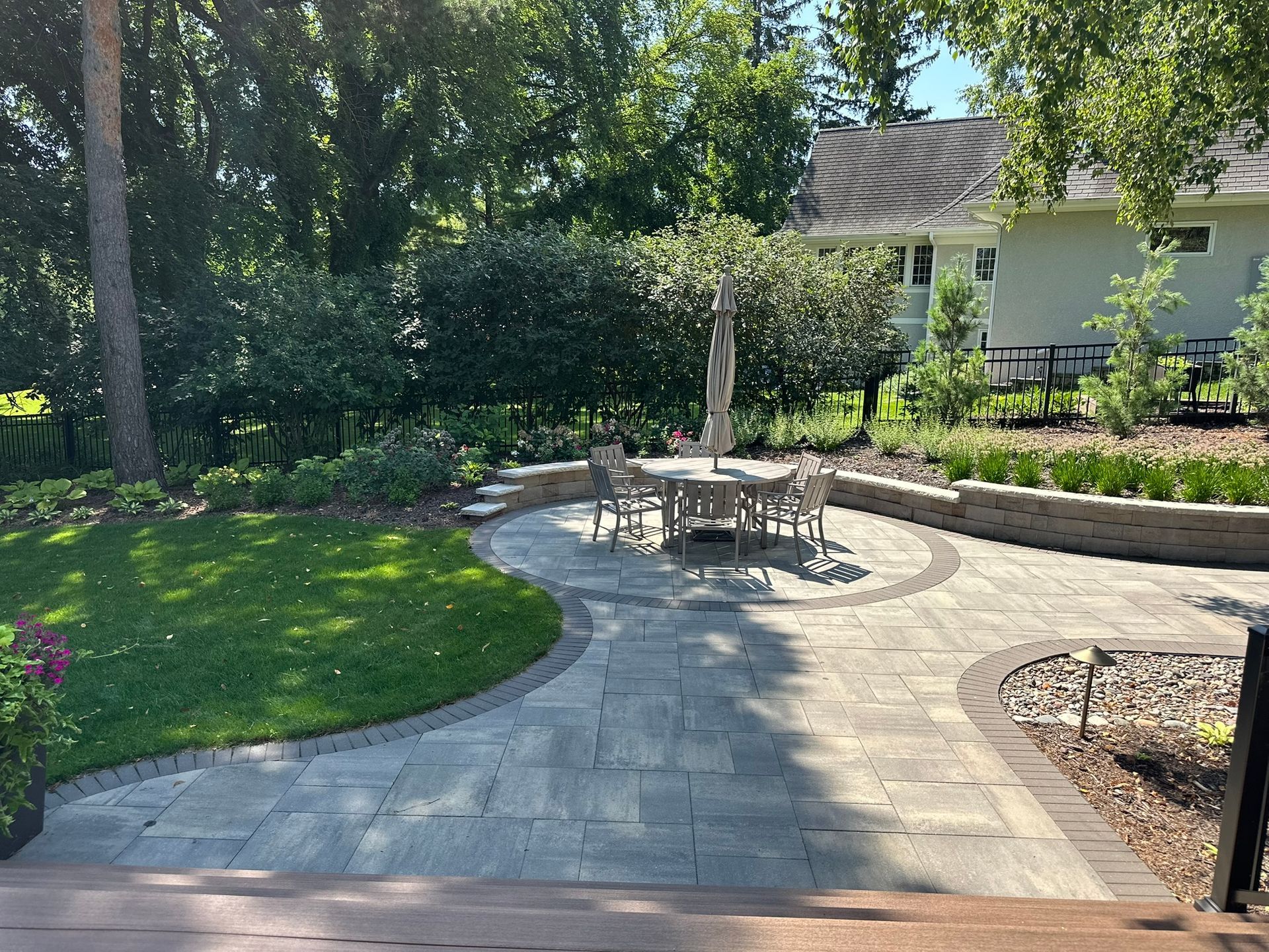 Perfect new gray paver patio with circular inlay for a round dining table and beautiful screen plantings behind a seating wall in Minnetonka MN designed by KG Landscape 