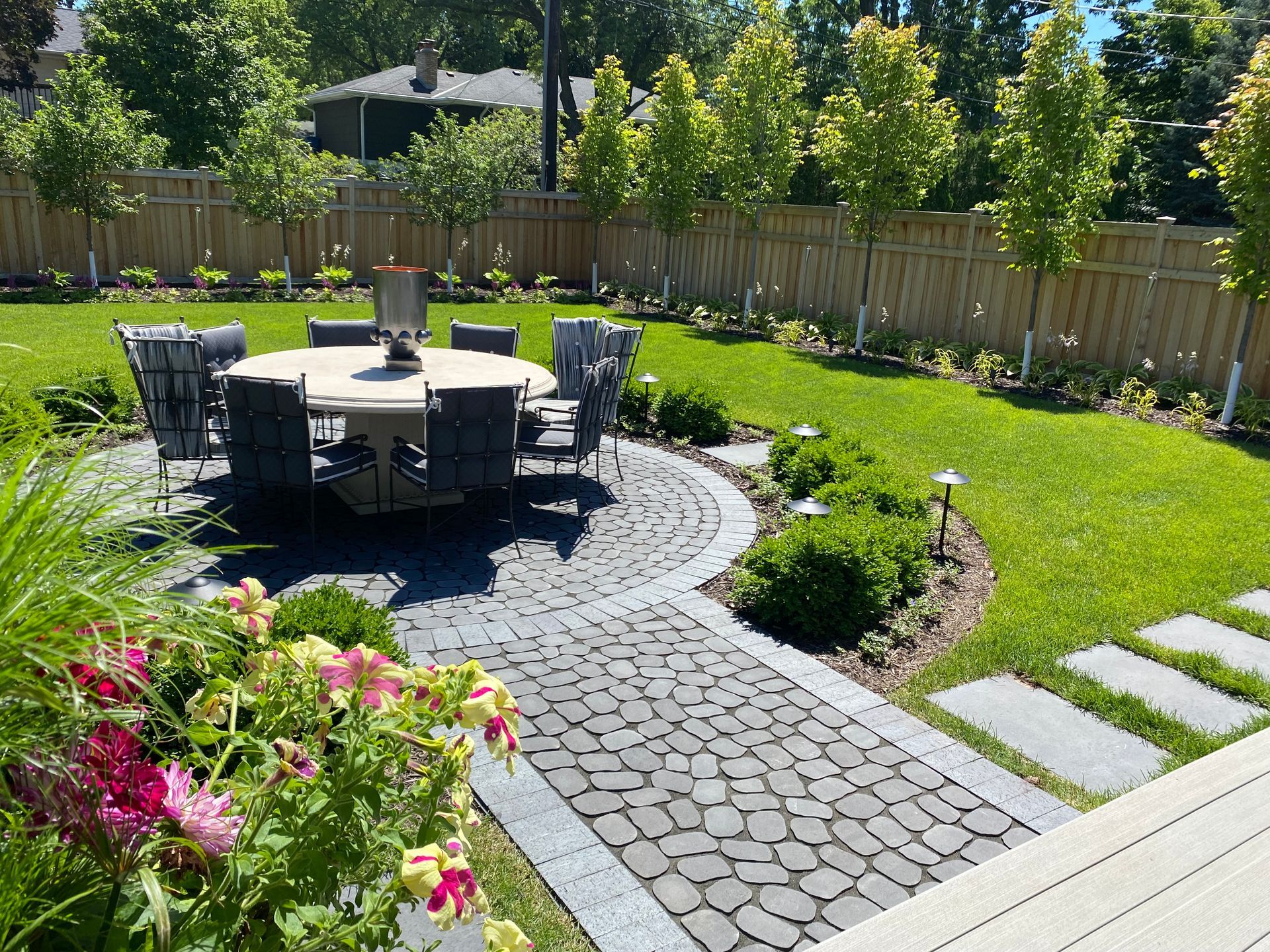 gorgeous backyard landscaping design KG landscape outdoor living space Edina MN inspiration ideas row of trees privacy cedar fence plantings table chairs stepping stones modern colorful 