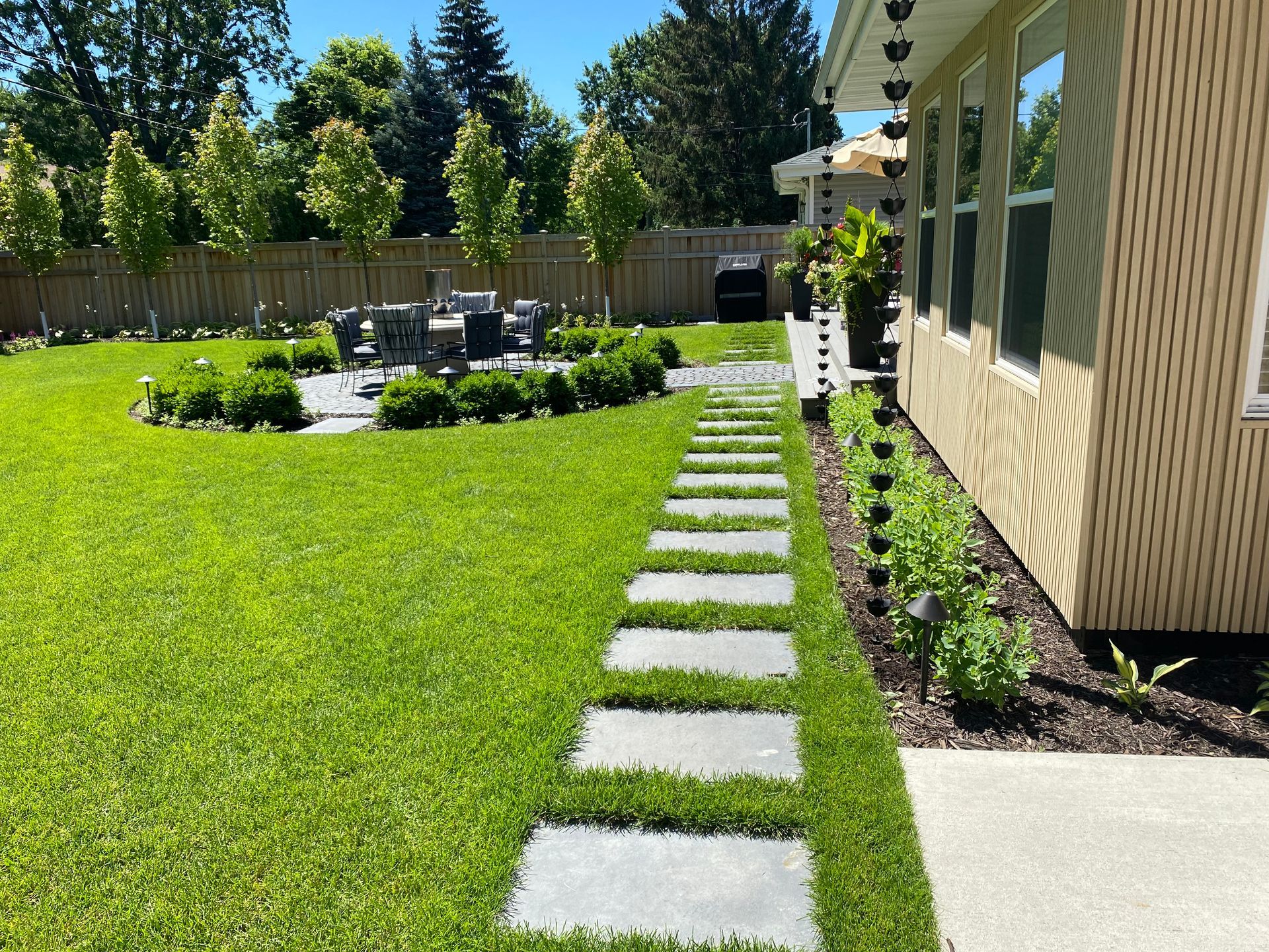 perfect backyard landscaping design KG landscape outdoor living space Edina MN inspiration ideas row of trees privacy cedar fence plantings table chairs stepping stones modern colorful boxwoods