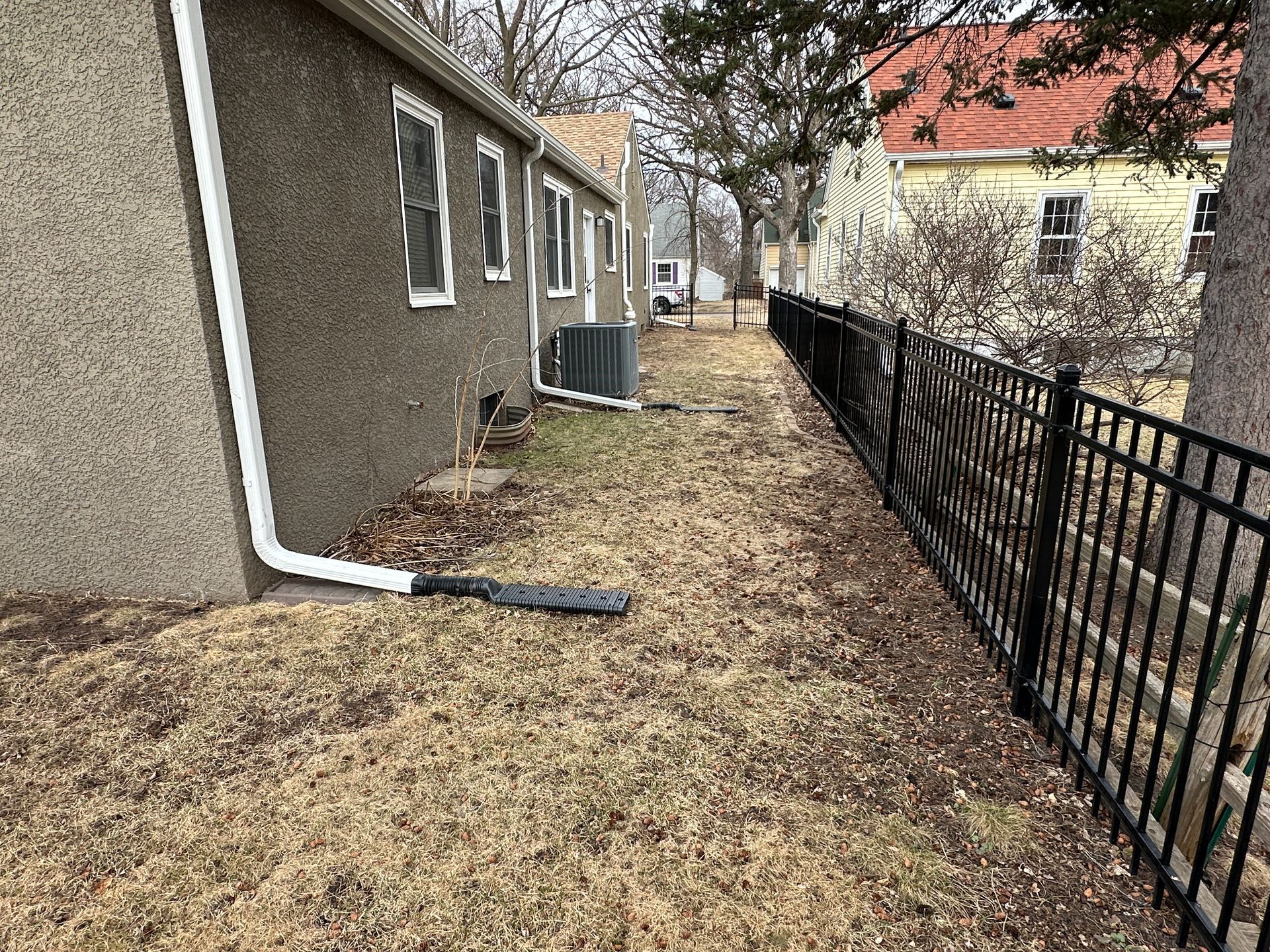 A picture of the side of a house with downspouts jutting into the yard.