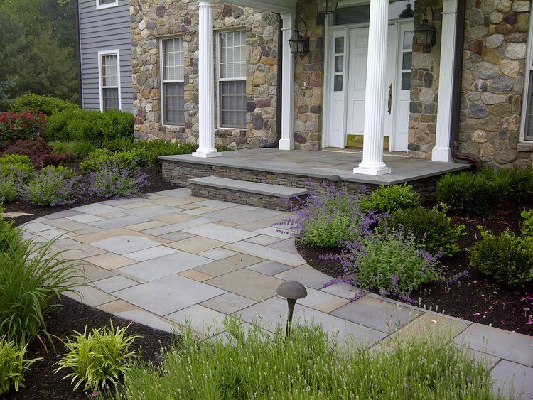 A stone walkway leading to a house surrounded by trees and bushes.