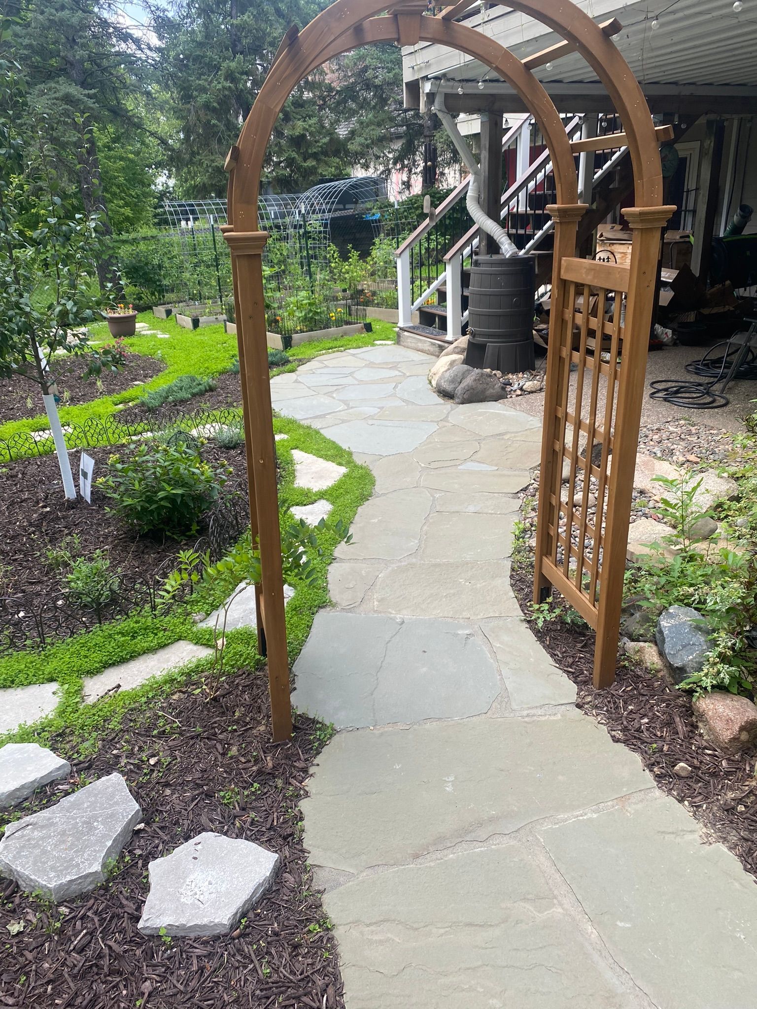 A stone walkway leading to a house surrounded by trees and bushes.