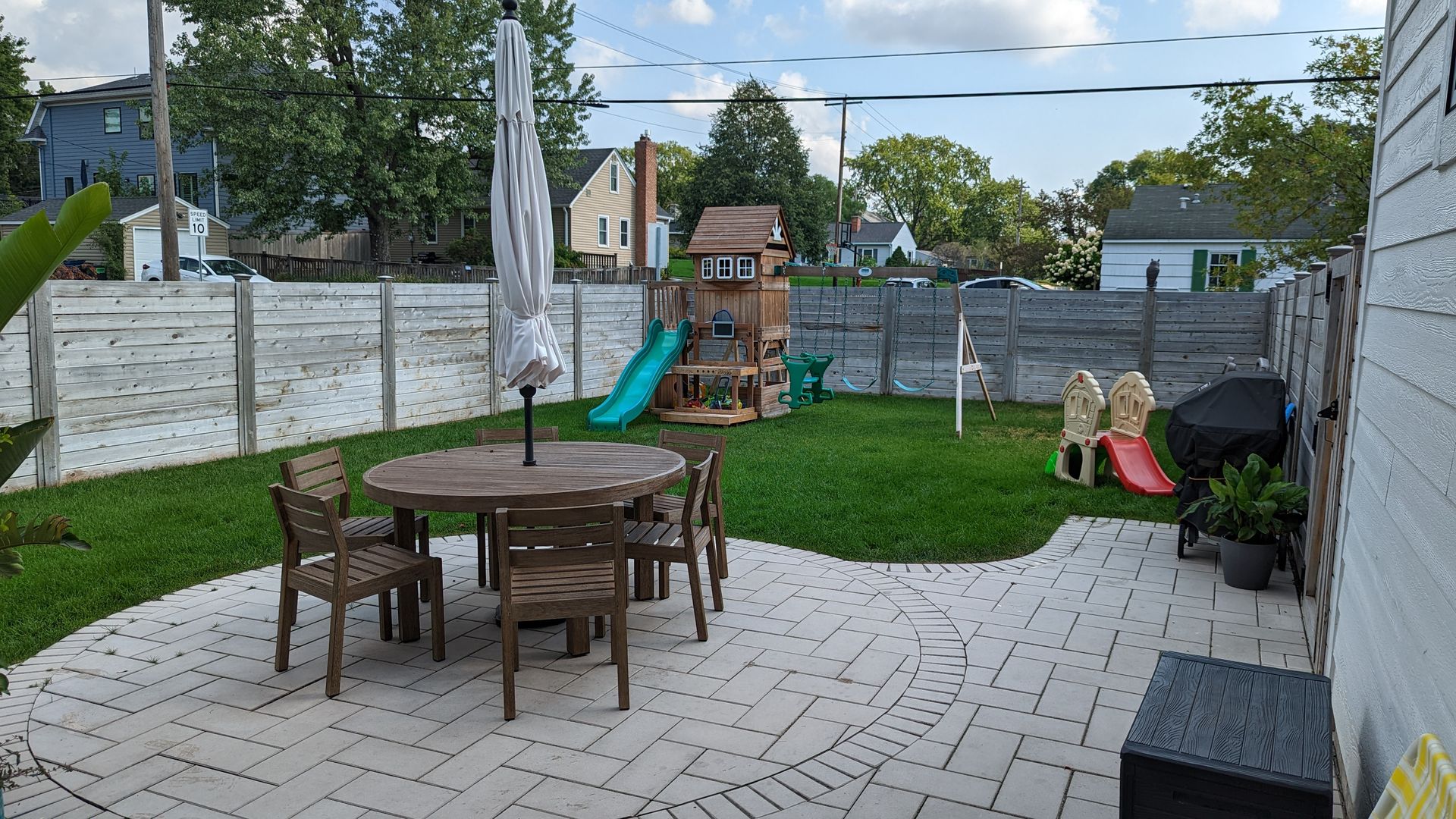Circular patio space for round table in nice backyard with green lawn in Edina, MN including a kids play set. 
