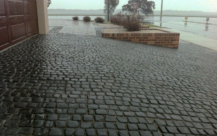 A brick driveway in the rain with a garage door in the background.