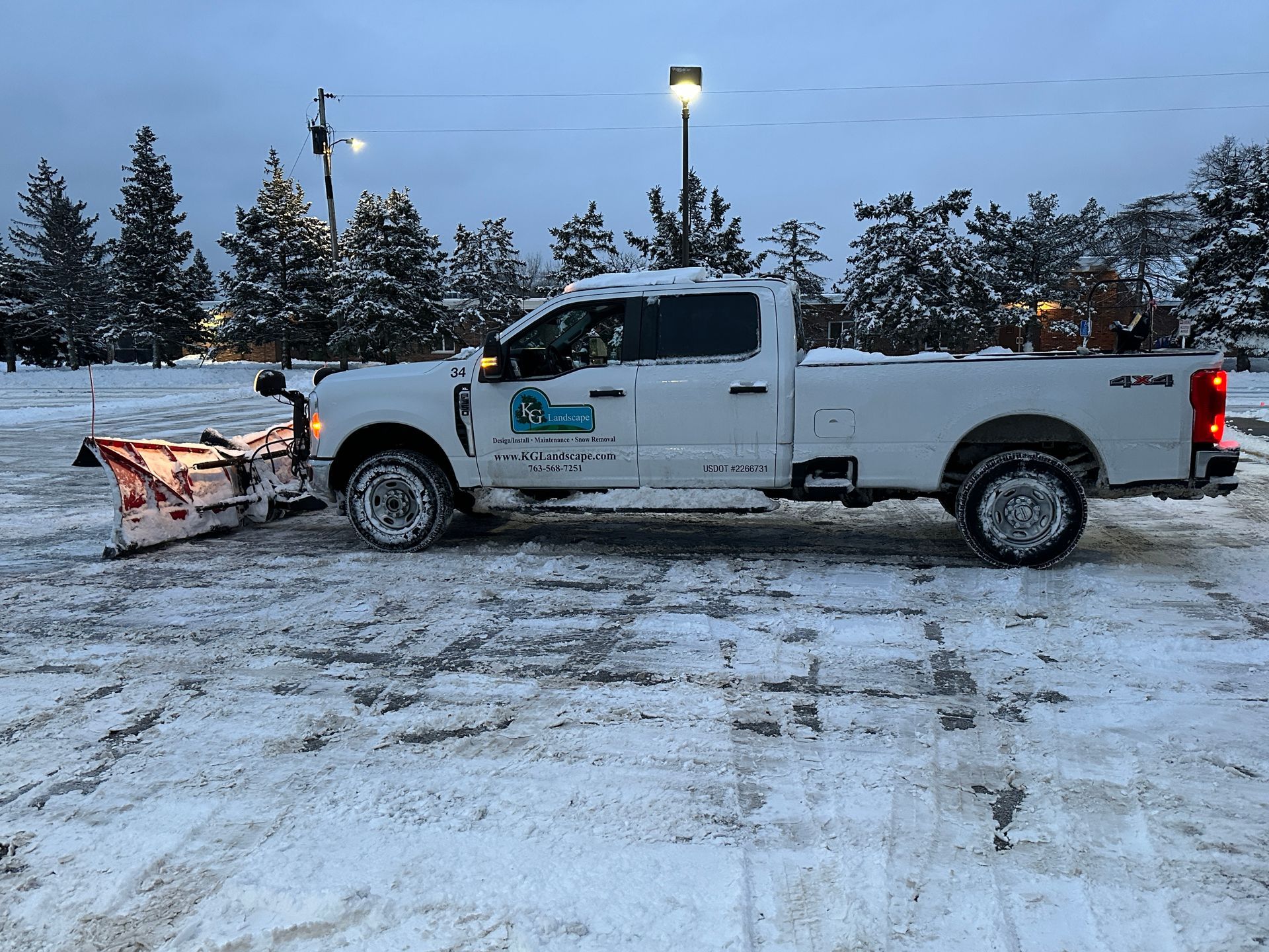 Snowplow clearing a snow-covered road lined with trees and bushes on a winter day.