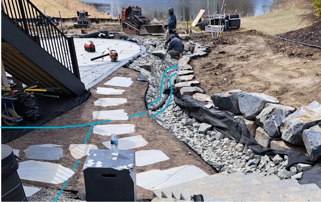 The blue line highlights the underground drainage pipe carrying sump pump discharge from the side yard as well as from another downspout, downhill into a dry creek bed on this Plymouth project.