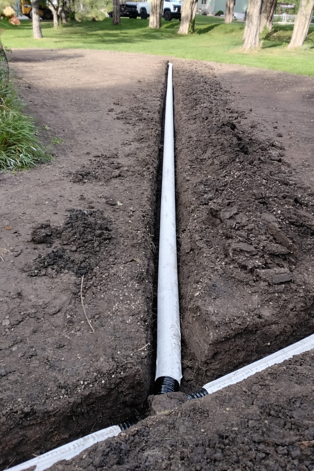 Drain tile being installed in graded lawn space in MN by KG Landscape using perforated pipe with a white silk sock cover 