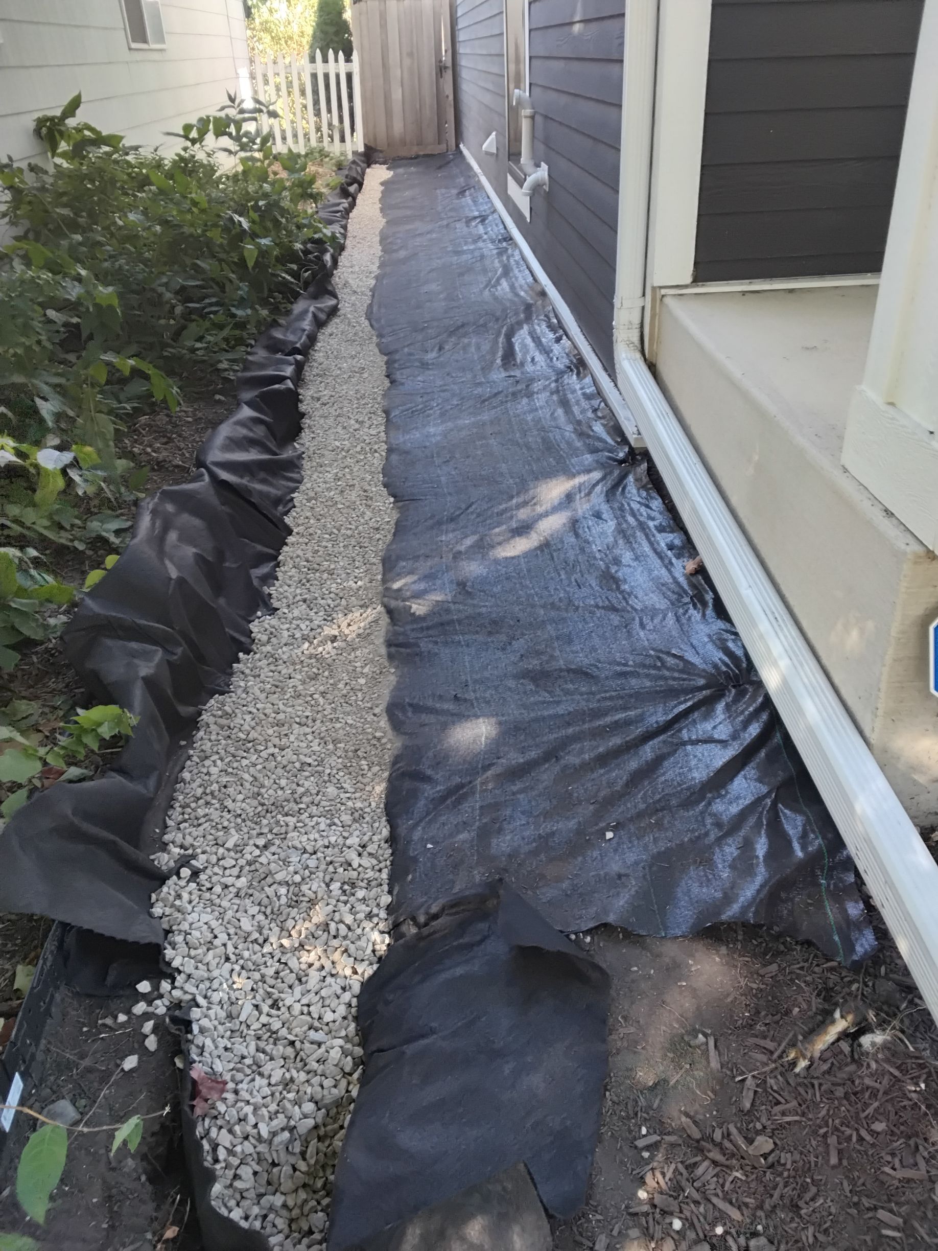 French drain being installed in narrow side yard in Minneapolis MN with black fabric liner below