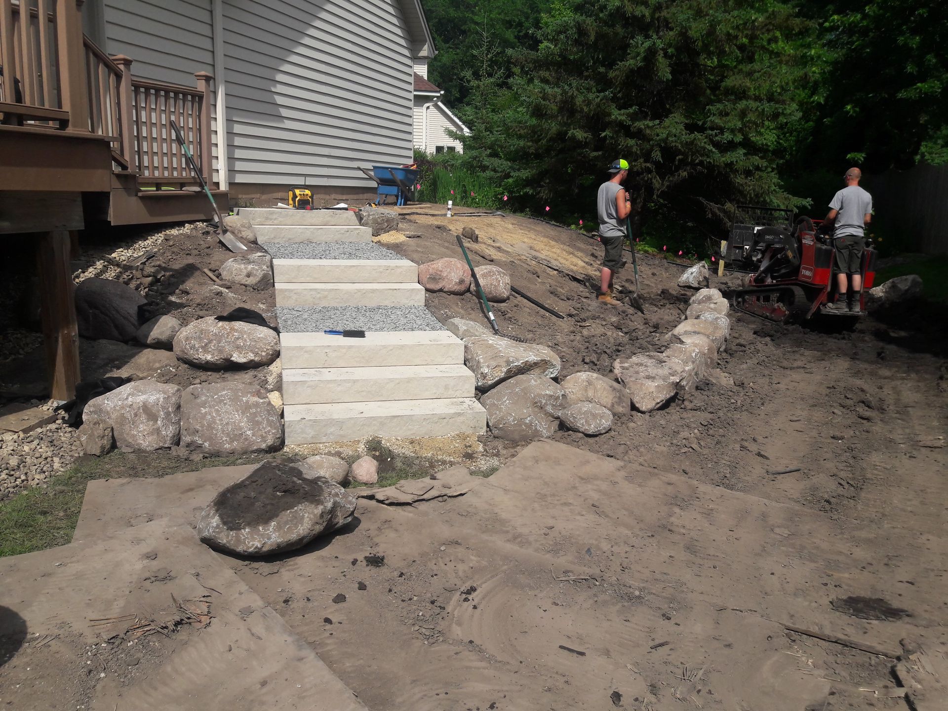 New Hillside landscaping area with steps being installed  by crew with boulder wall and plantings on the slope 