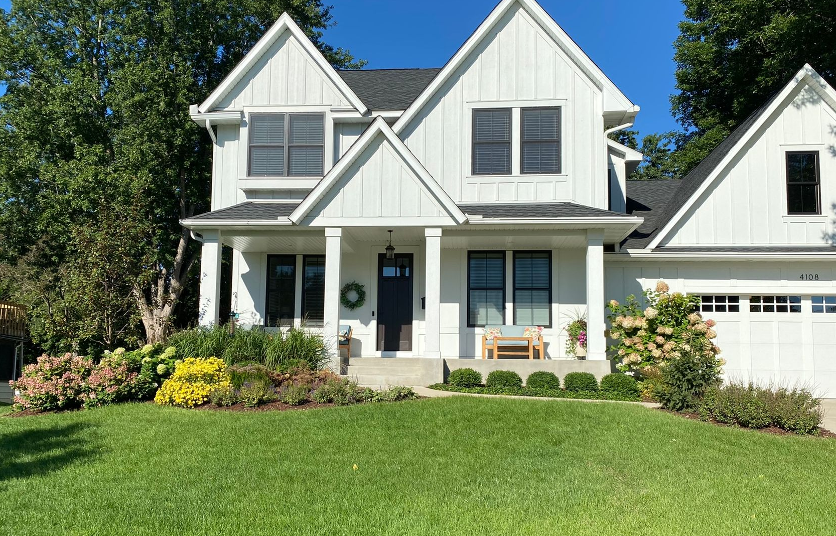 Front yard designed landscaping with beautiful flowers and shrubs large white house