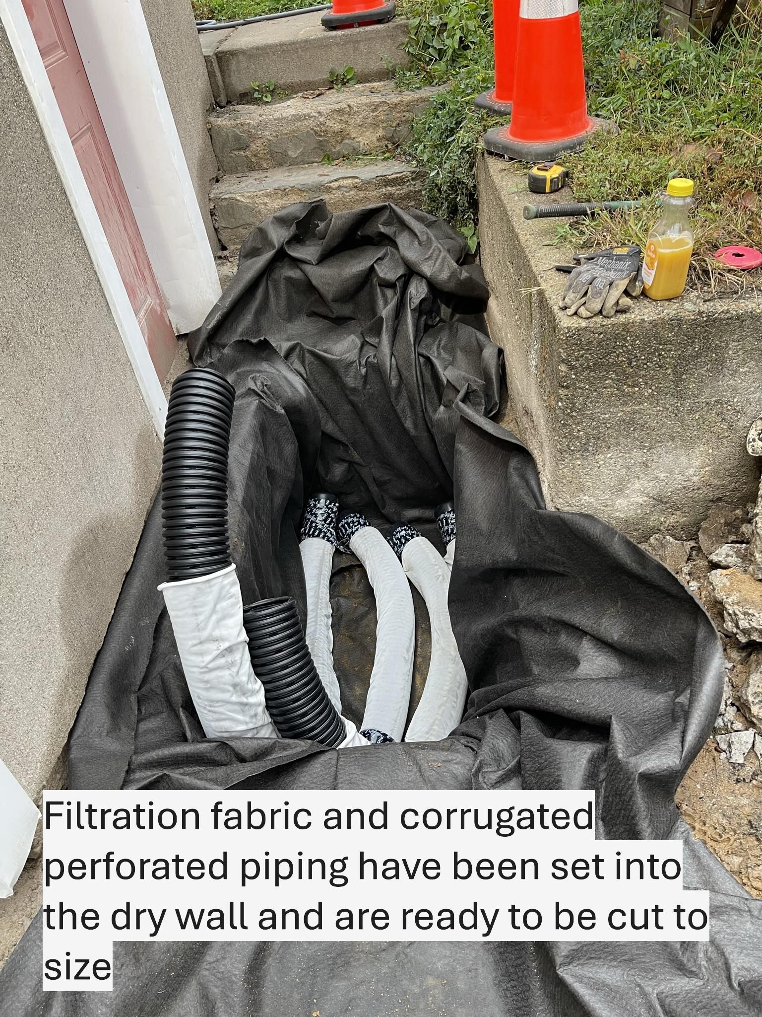 Black filtration fabric and perforated piping ready to be cut, set near a retaining wall.