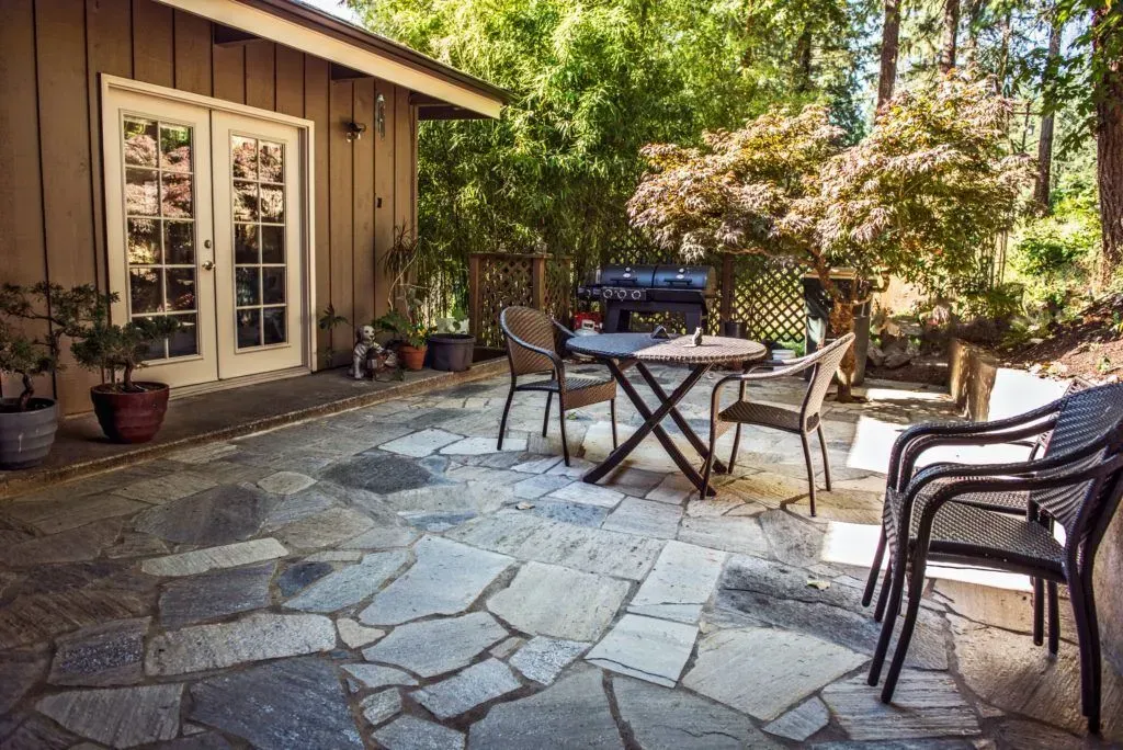 A stone patio with a table and chairs in front of a house.