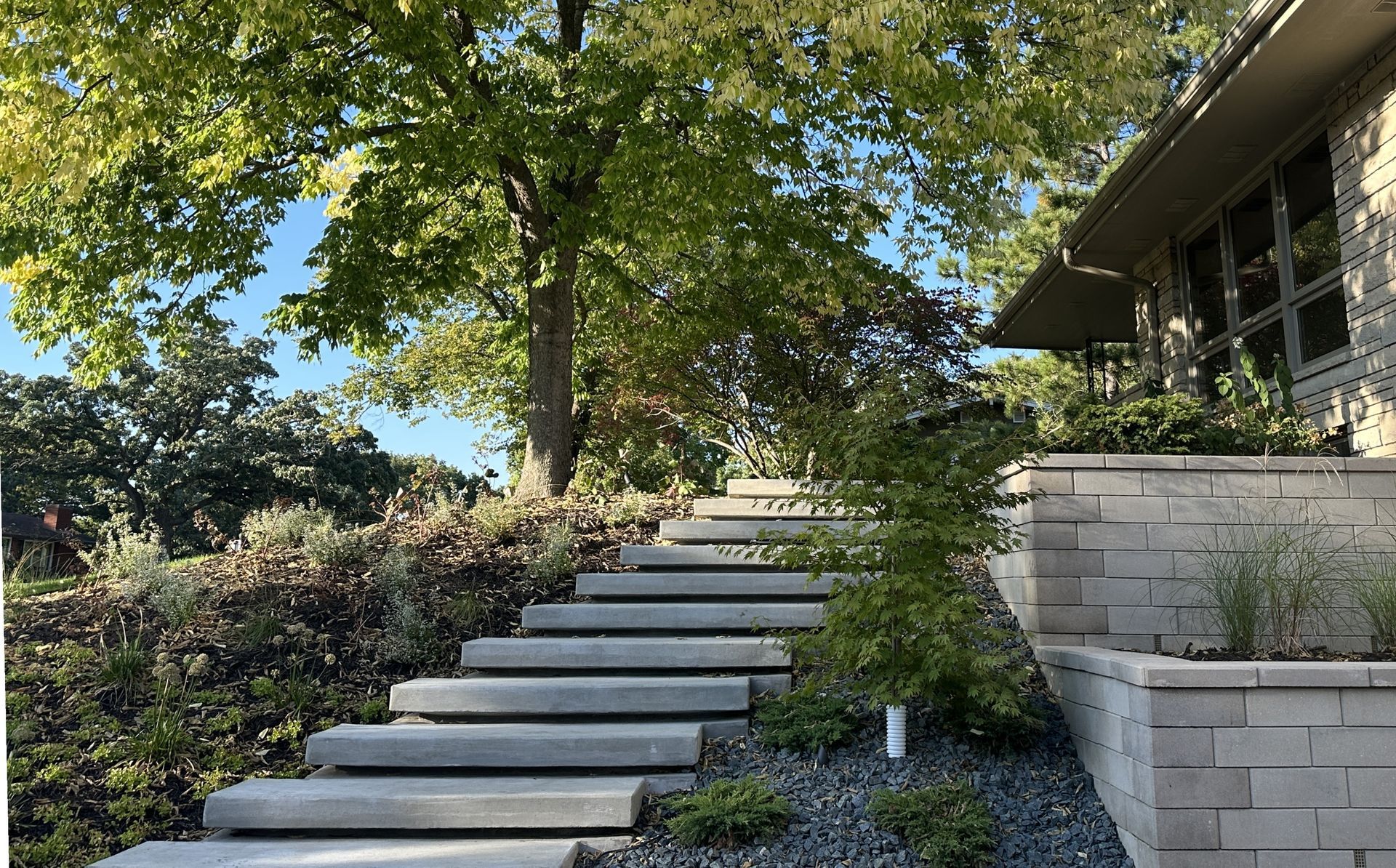 Concrete steps leading up a sloped yard, near a house with brick planters.