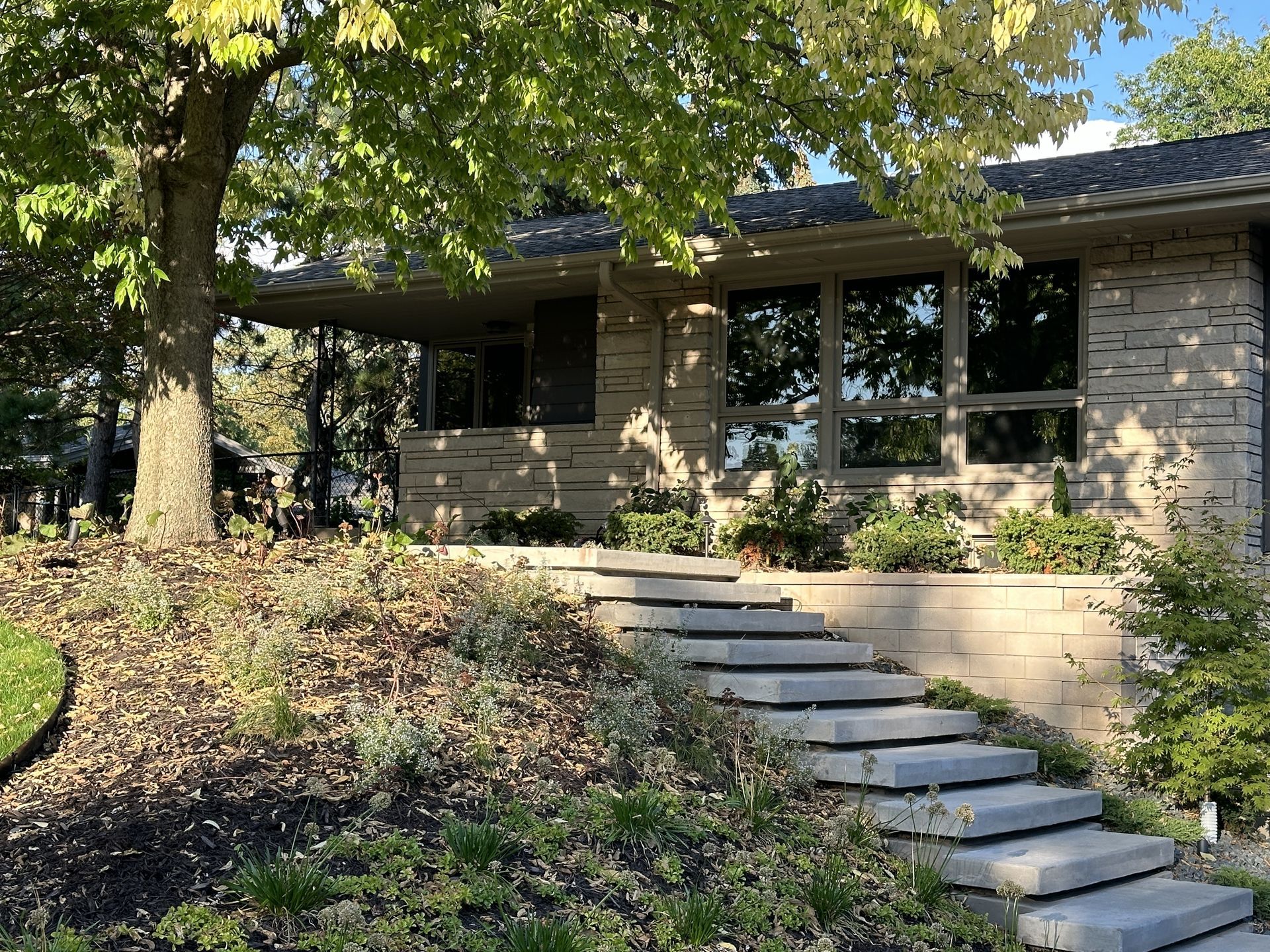 A stone house with steps leading up to the front door, surrounded by landscaping and a tree.