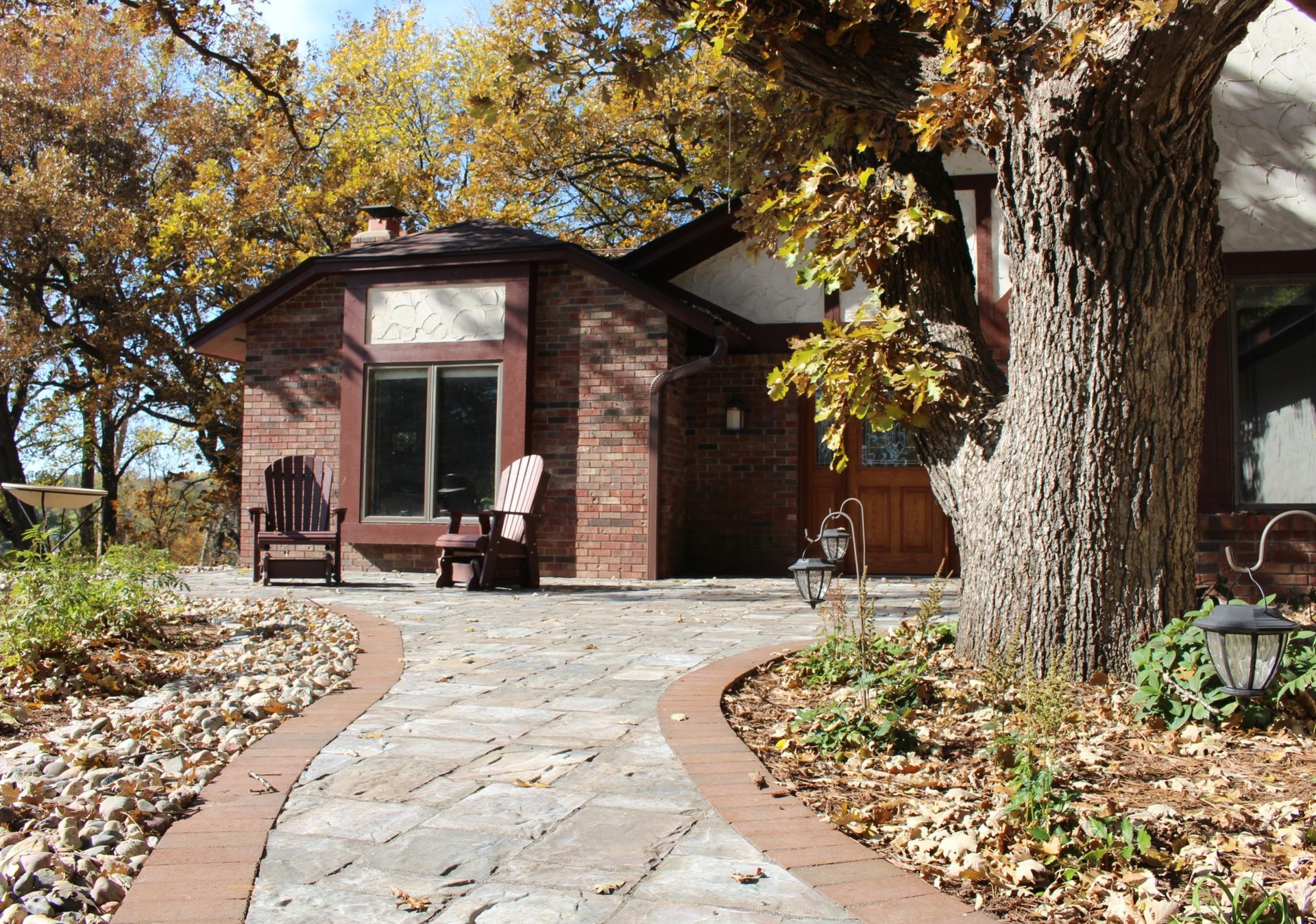 Brick house with stone path, two chairs, and fall foliage.