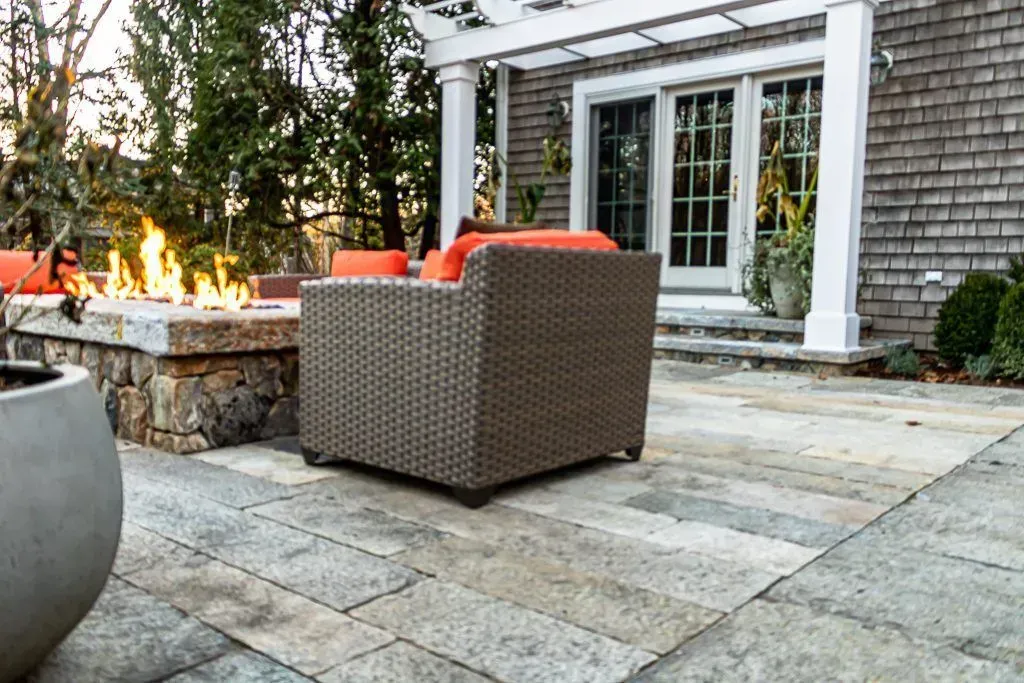 A patio with a fire pit and chairs in front of a brick house.