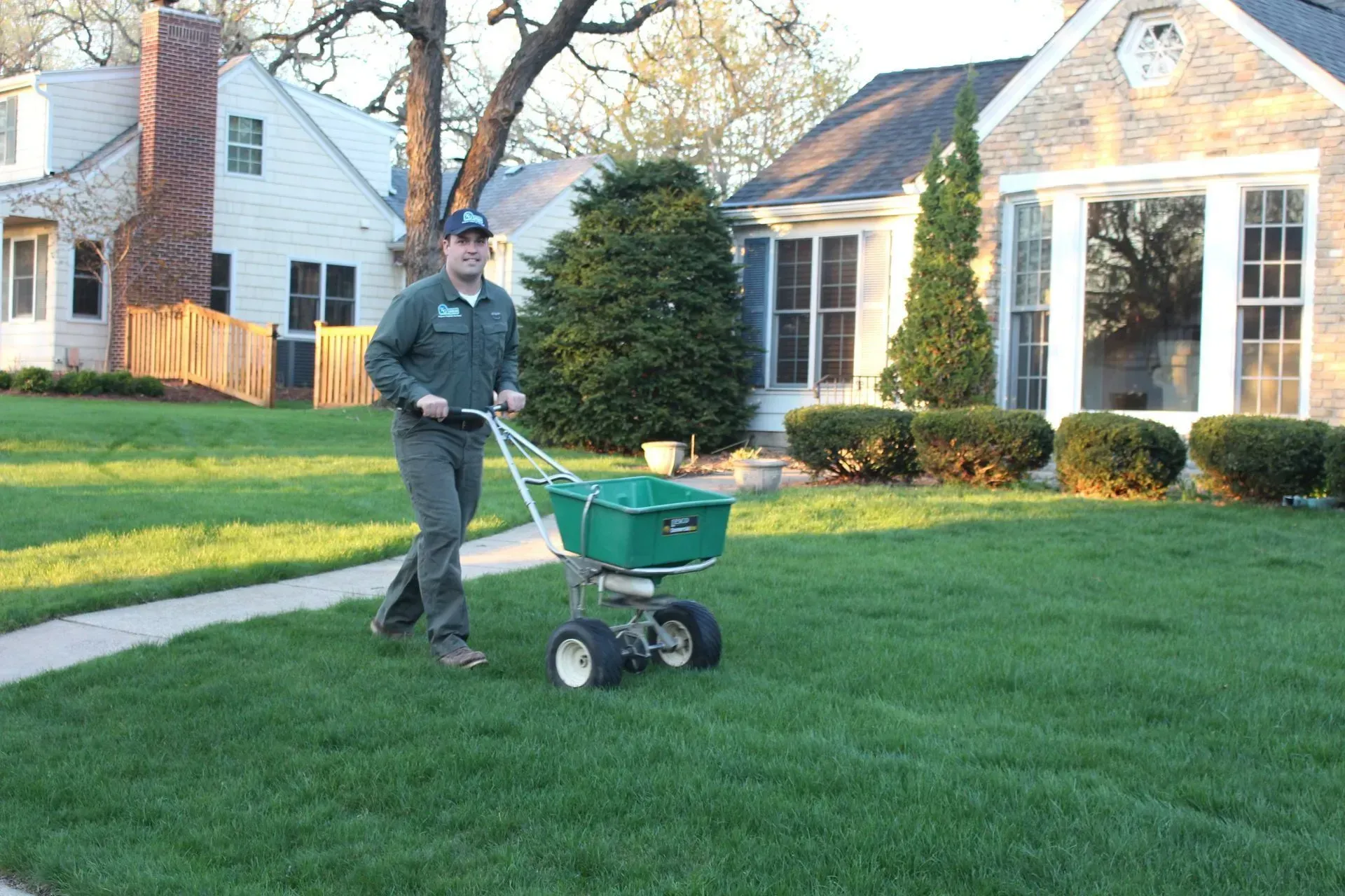KG crew member applying lawn fertilizer with spreader in a Minneapolis lawn 
