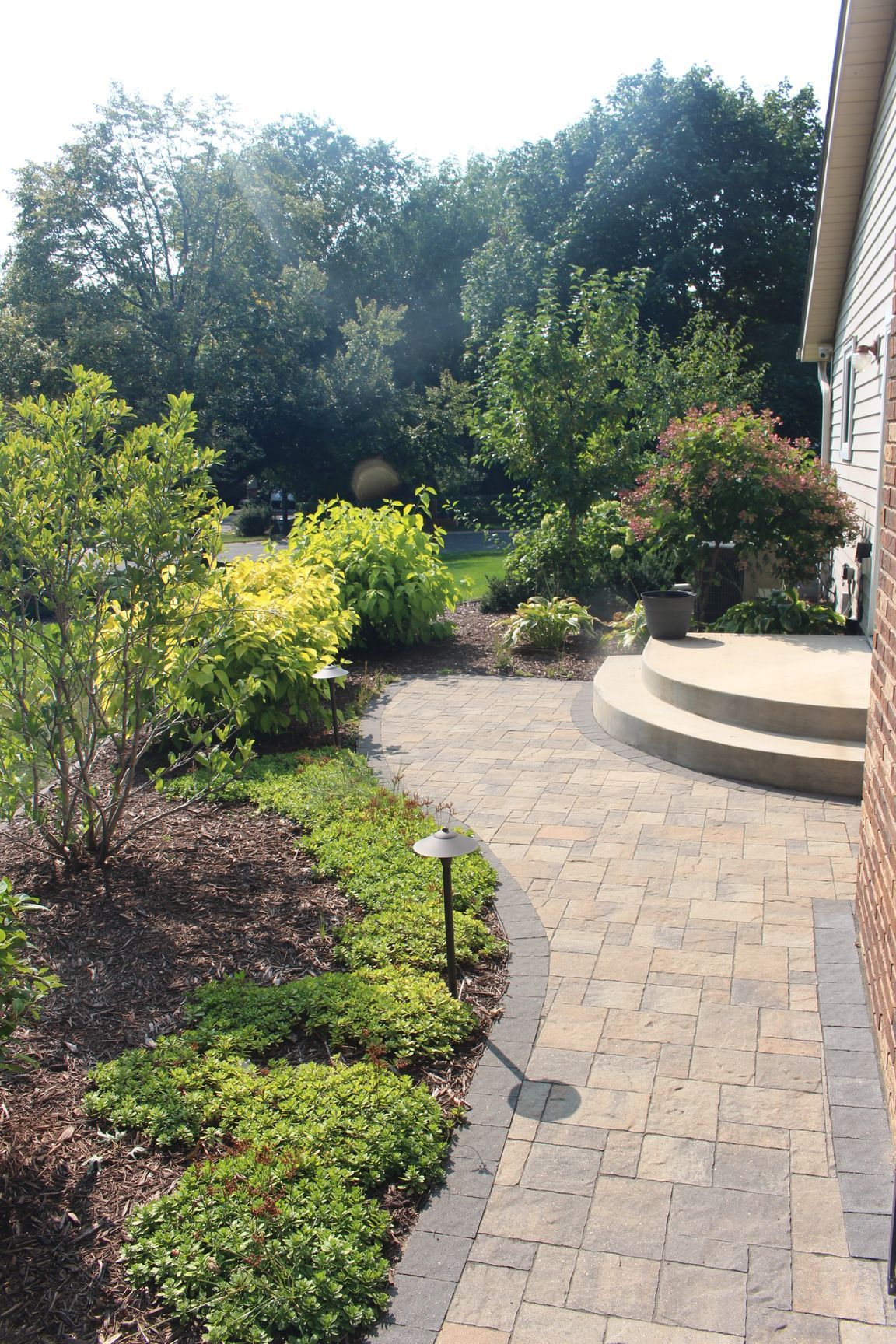 Custom quarter circle concrete landing steps with paver walkway out a sliding door Shoreview with plantings and pathway light MN KG Landscaping Company 