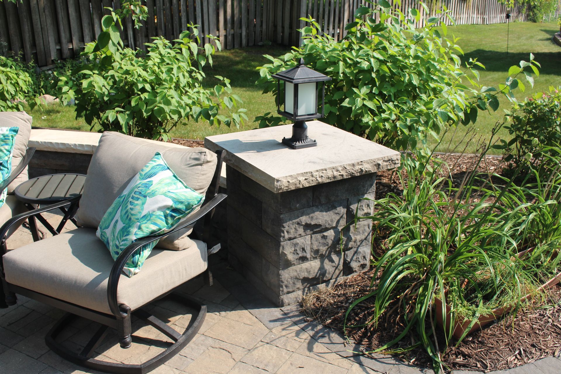 Stone block column with limestone capstone sitting wall around paver patio with light fixture on top chairs backyard pavers Shoreview MN KG Landscaping Company 