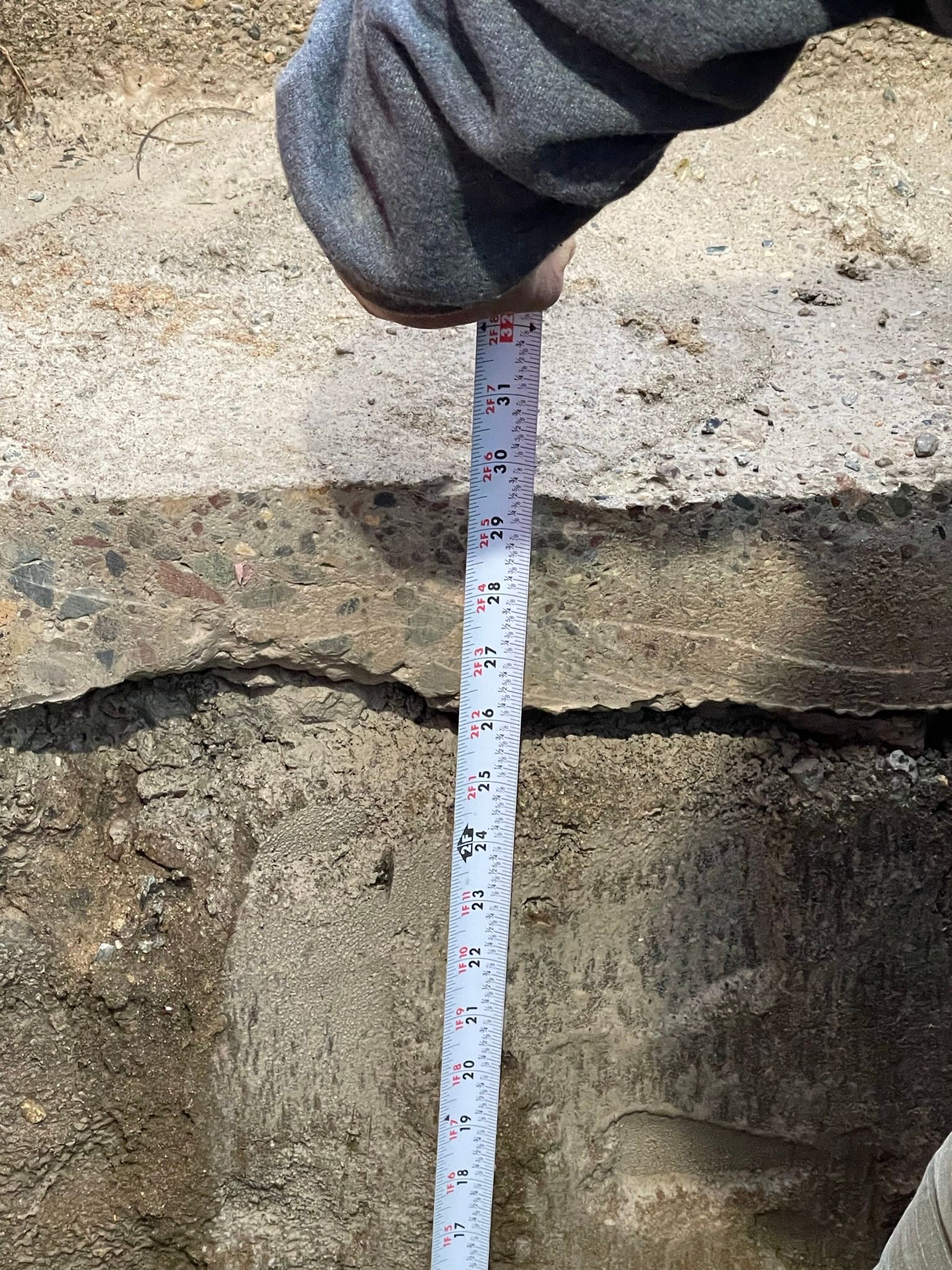 Person measuring depth of a crack in concrete with a tape measure.