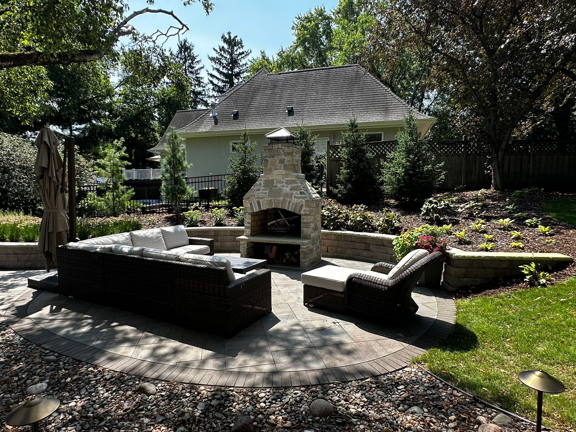 New backyard patio with outdoor living space with nice lounge seating sofa and chairs with fireplace and wall and birch tree in Minnetonka MN designed by KG Landscape 