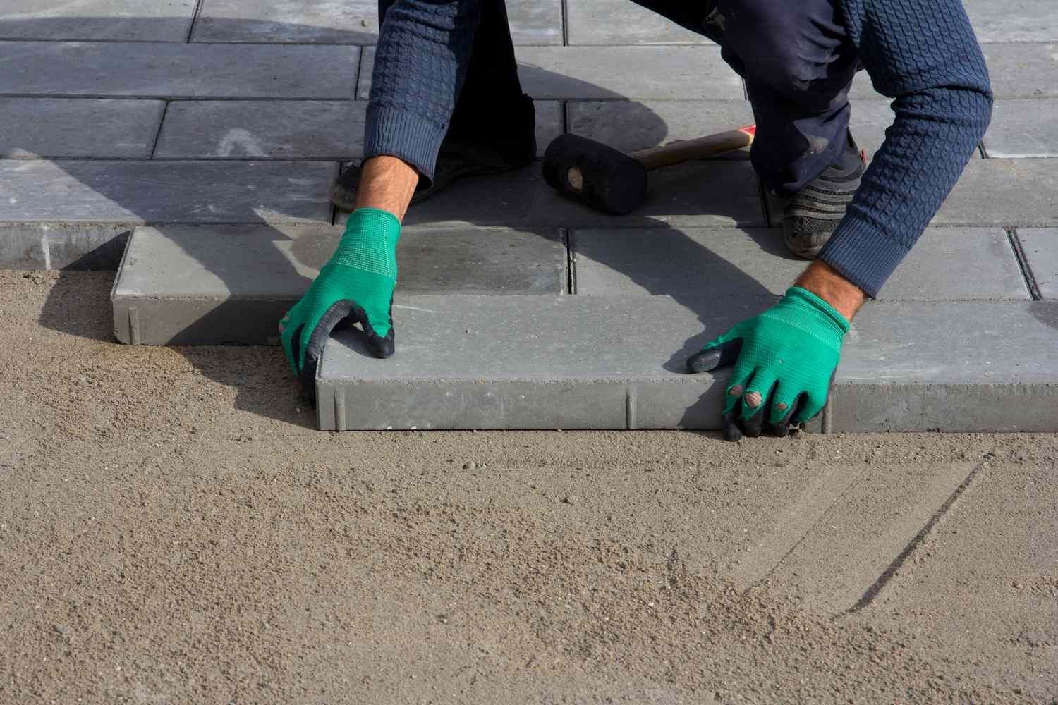 A person wearing green gloves is laying bricks on the ground.