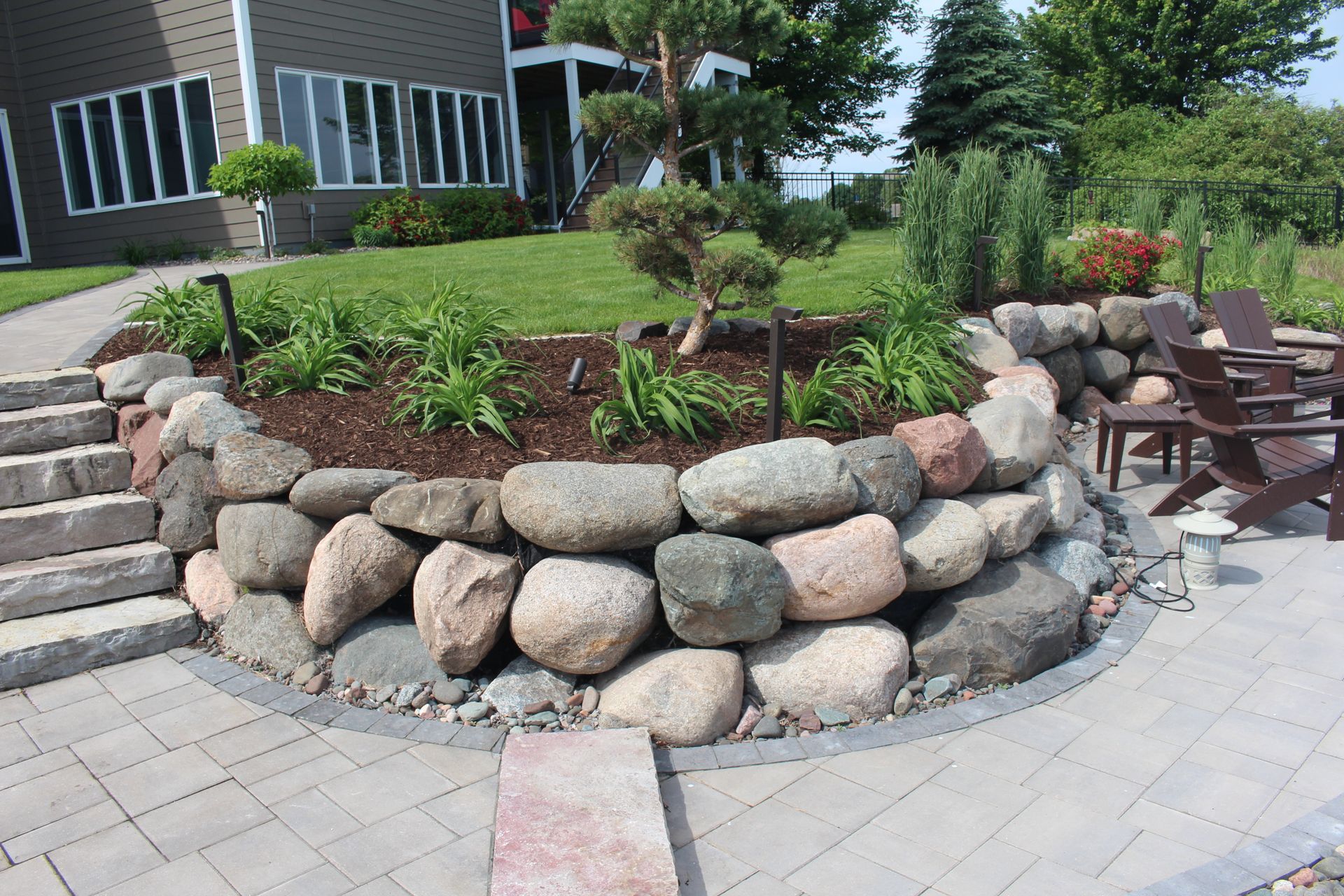 Landscaping seating space with fire pit near water shoreline paver patio carved into hillside with boulders steps plantings lighting Blaine MN KG Landscape  