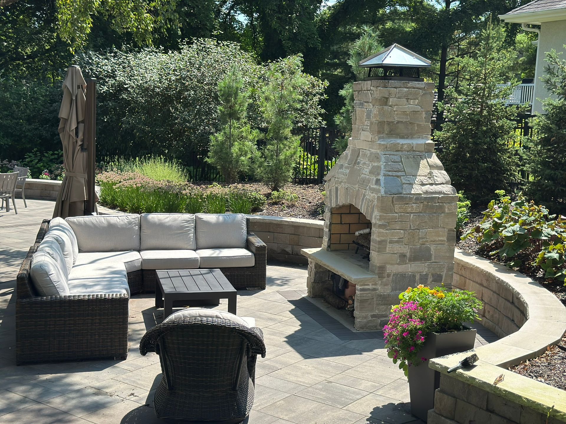 After backyard patio with outdoor living space table and fireplace and wall and birch tree in Minnetonka MN designed by KG Landscape 