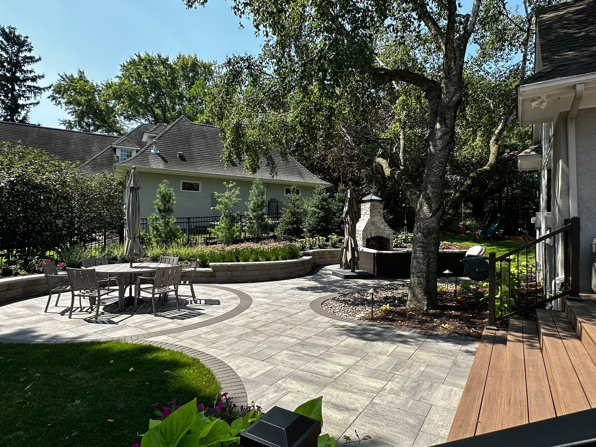 New backyard patio with outdoor living space table and fireplace and wall and birch tree in Minnetonka MN designed by KG Landscape 