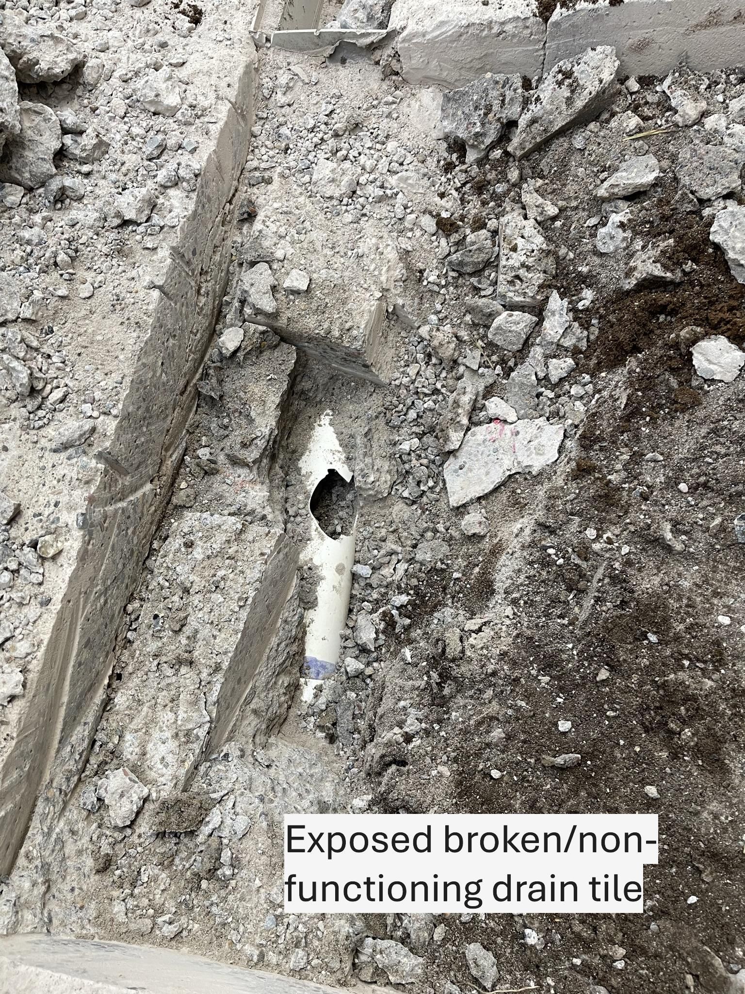 Exposed and broken white drain pipe in concrete rubble. Text identifies it as non-functioning.