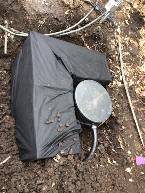 A black tarp is covering a metal object in the dirt