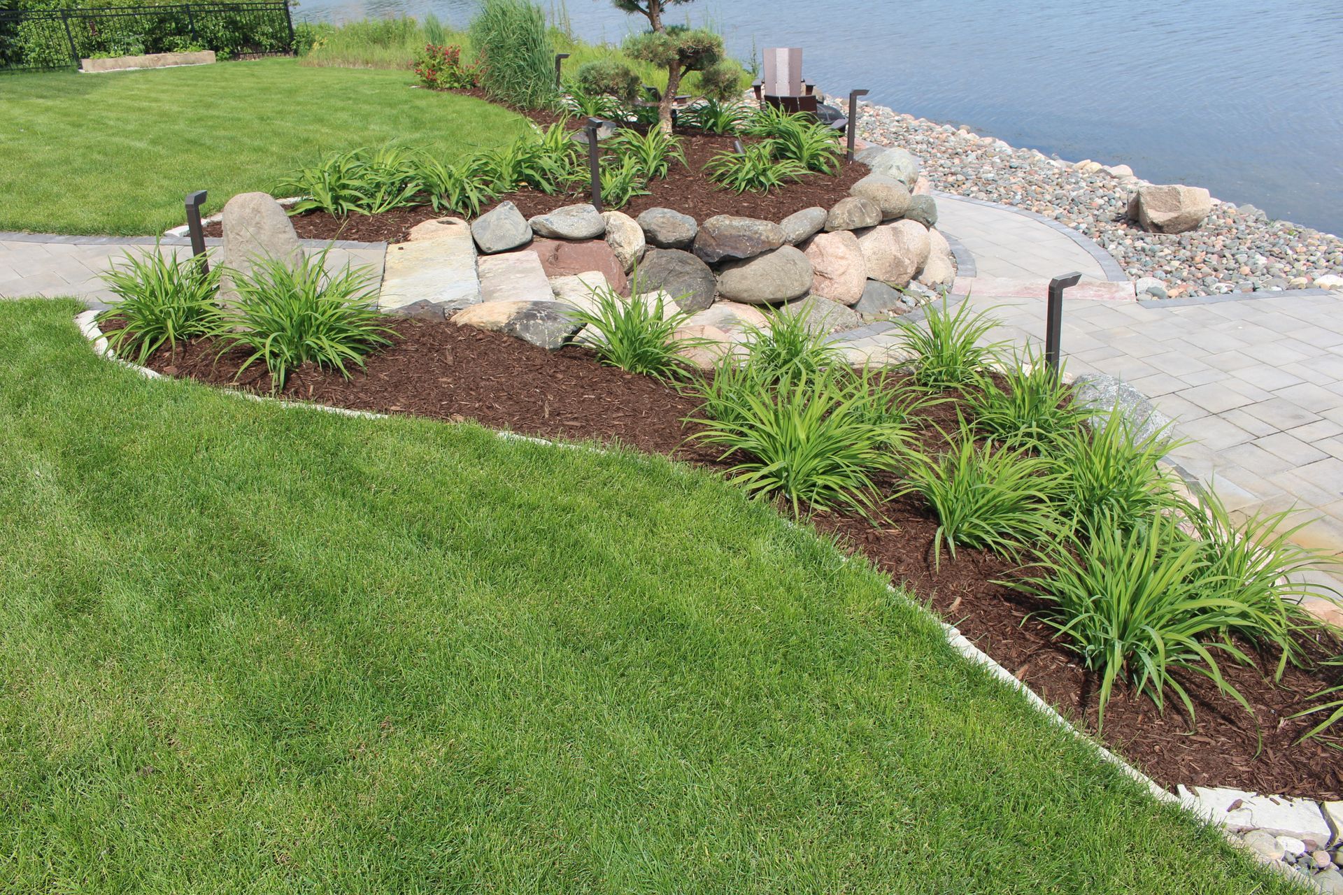 Landscaping patio space with fire pit near lakeshore with plantings steps stairs walkway pavers boulders lighting Blaine MN KG Landscape  