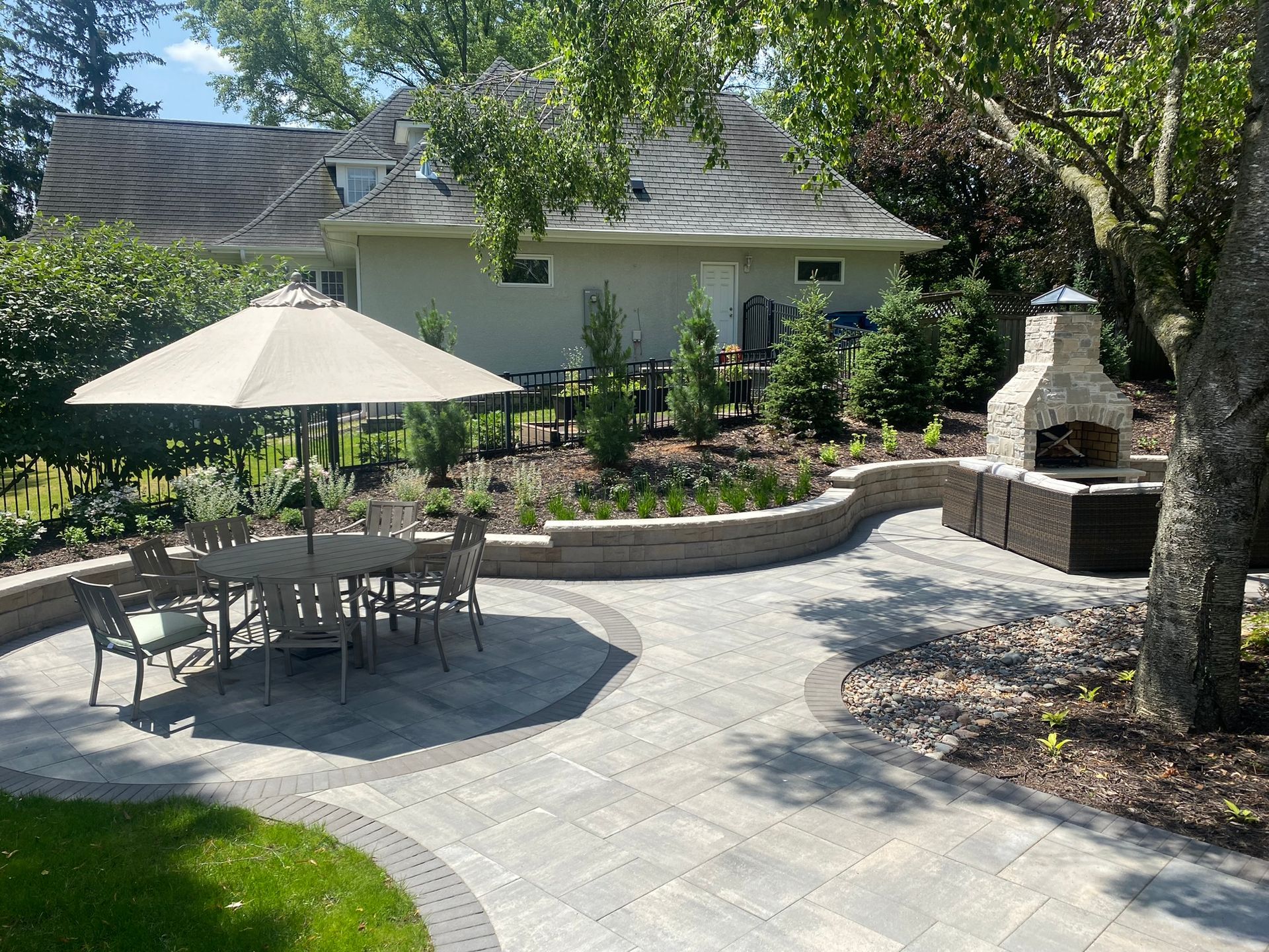 Patio design and installation example Minnetonka MN KG Landscape Curvilinear shape with gray pavers and black soldier course surrounded by a beautiful  sitting wall outdoor fireplace wicker furniture 