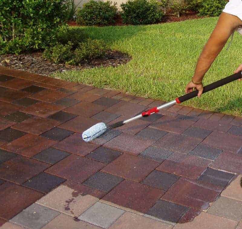 A person is painting a brick driveway with a roller