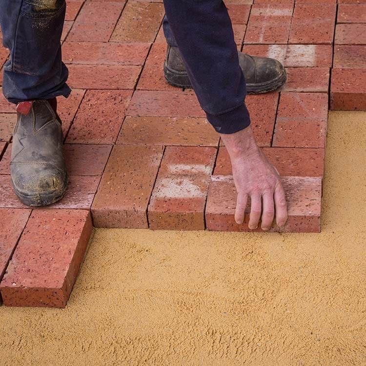 A person is laying bricks on a sandy surface