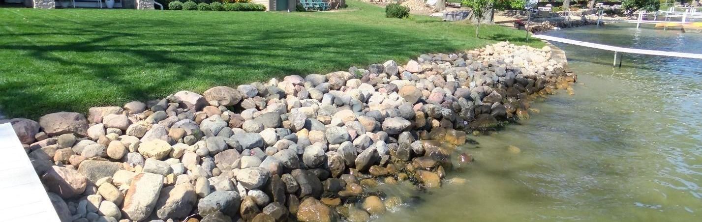 A large pile of rocks is sitting next to a body of water.