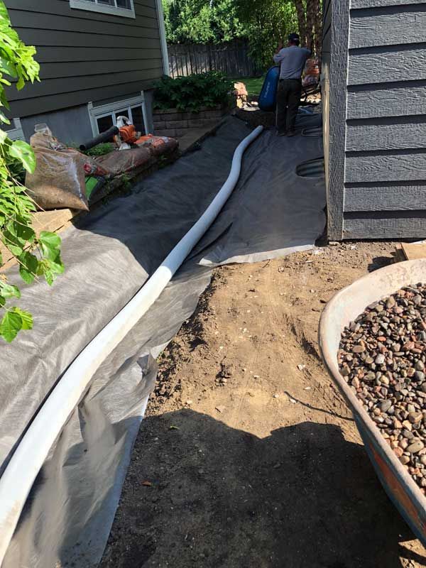 Foundation landscaping drain tile installed into carved out swale to direct water into dry well with 