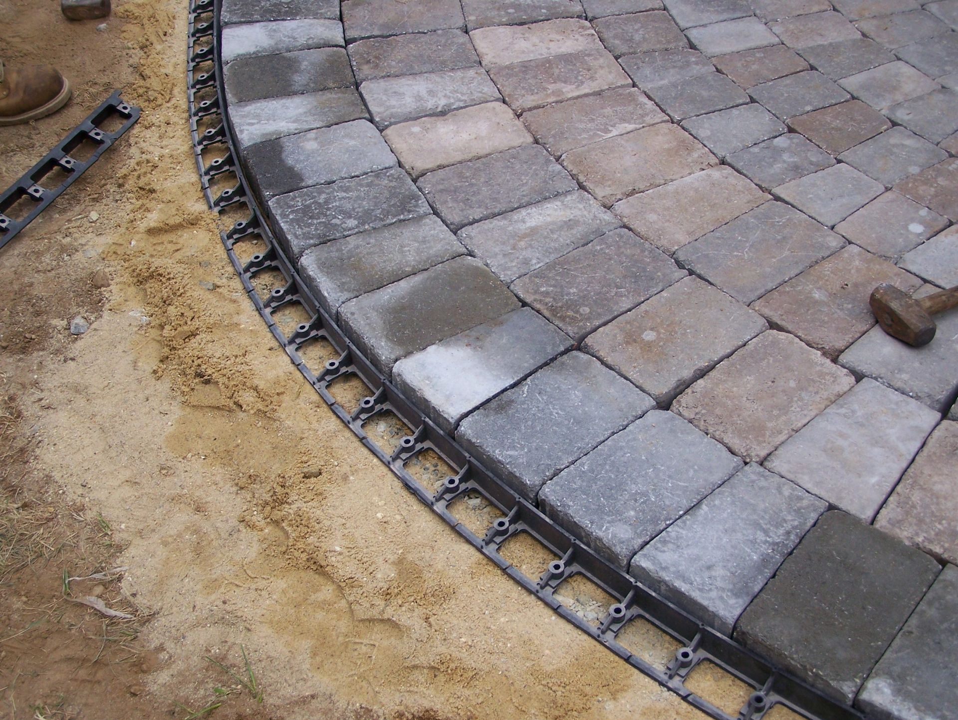 A brick patio is being built with a black edging