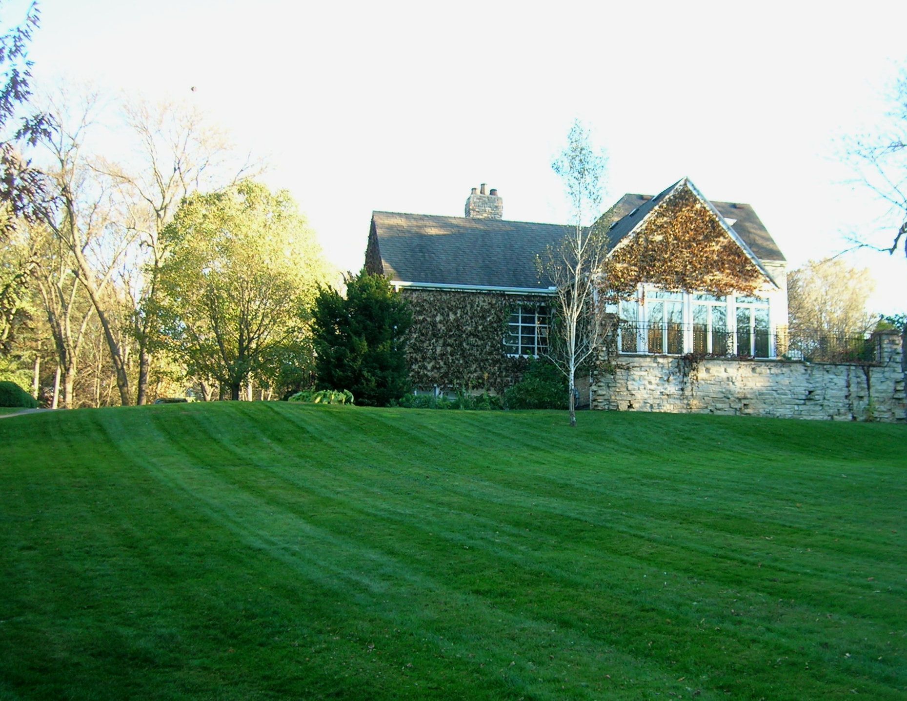 Lush green lawn and garden leading to a two-story house with a balcony, under a sunny sky.
