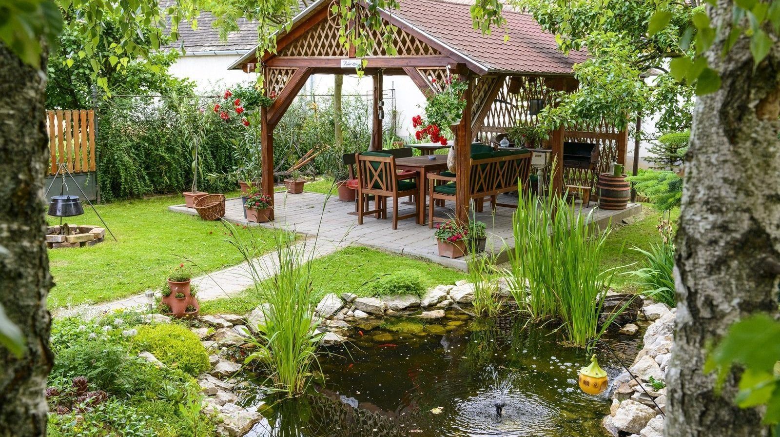 There is a gazebo in the middle of a garden with a pond in front of it.