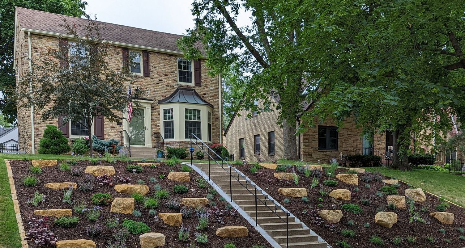 A large brick house with a lush green lawn and stairs leading up to it.
