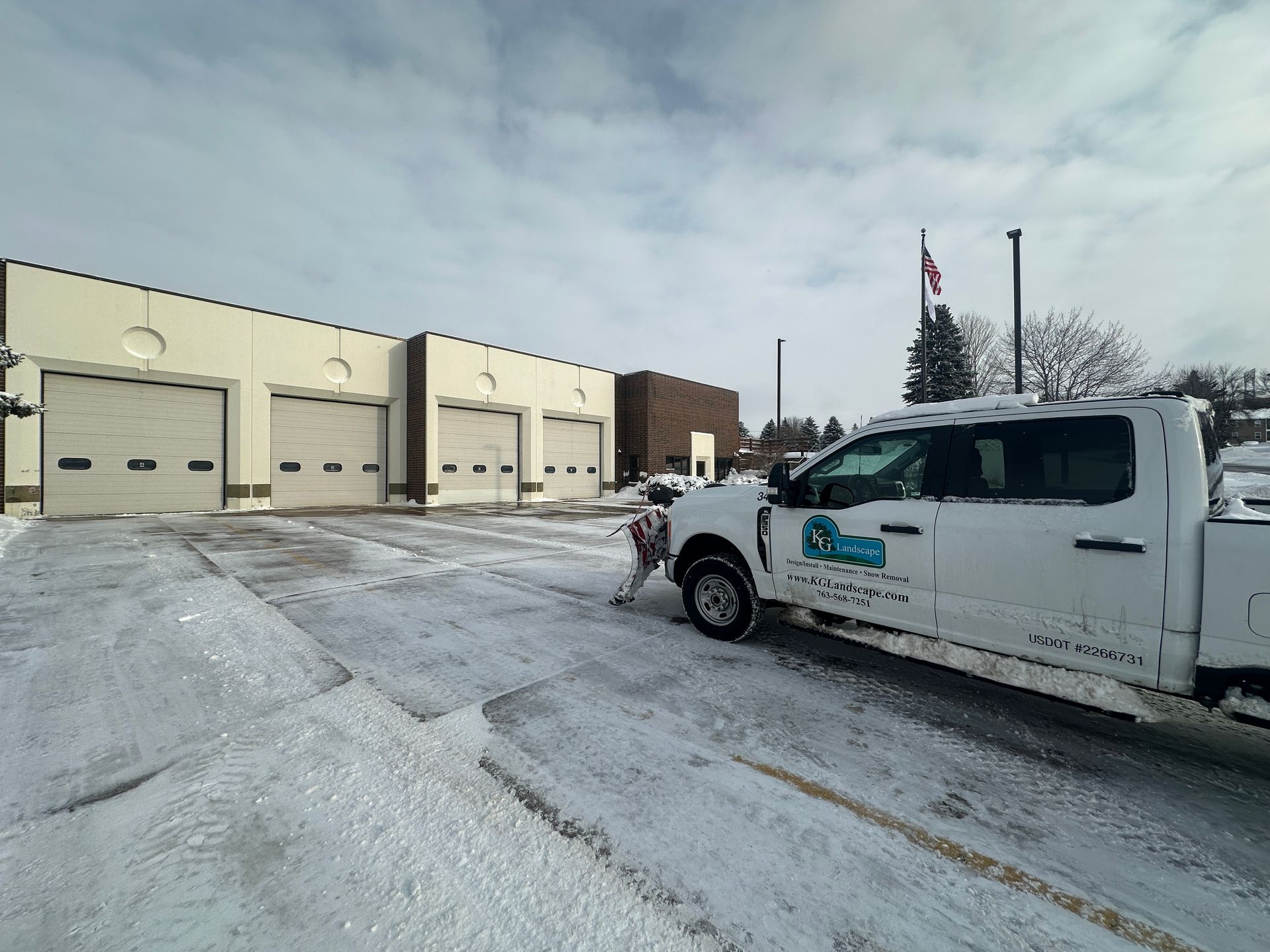 White truck with a red plow clearing snow from a snow-covered road in a wooded area.