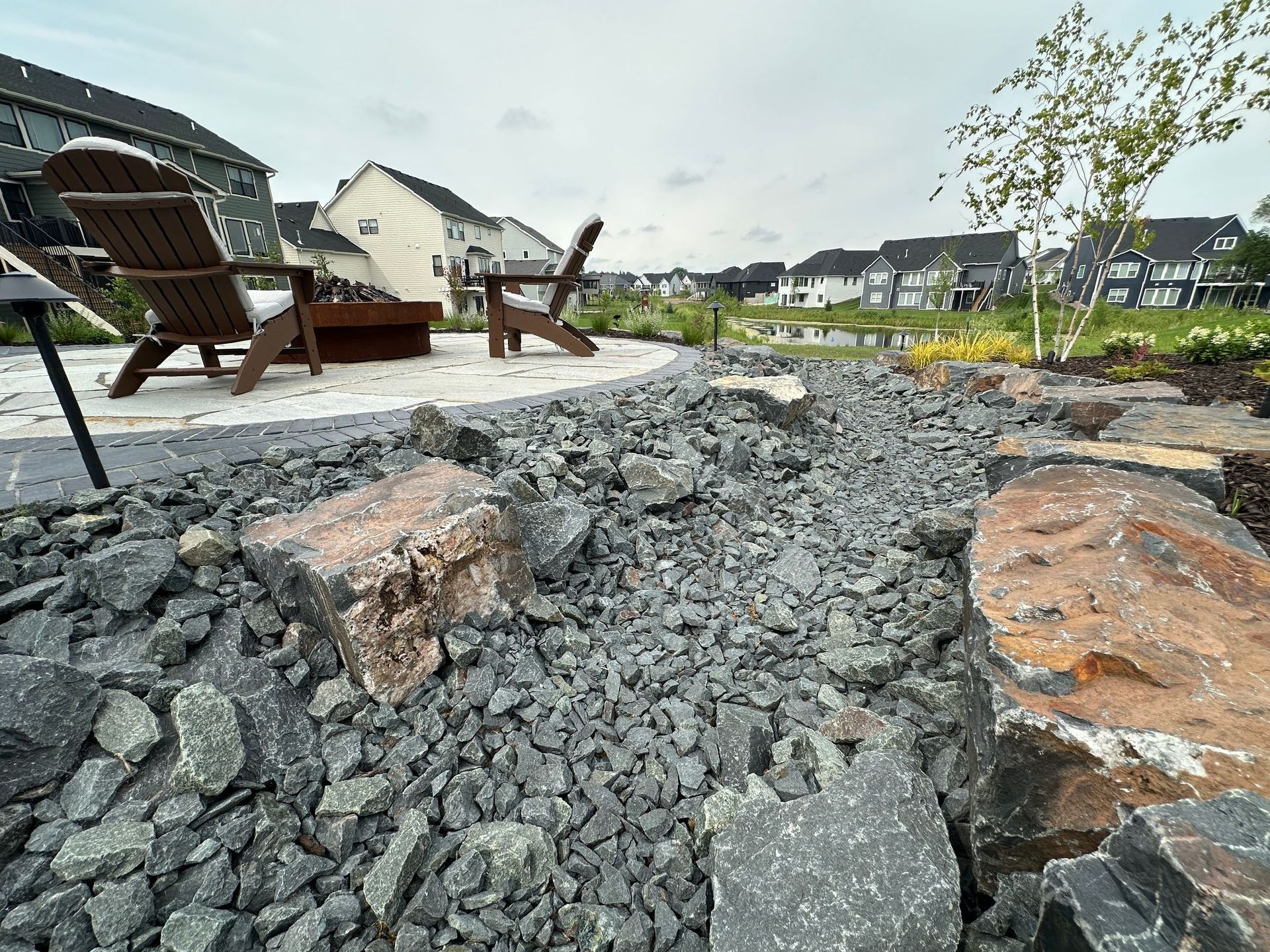 Dry Creek Bed Landscaping using Gray trap rock and boulders next to natural stone patio in backyard KG Landscape Plymouth MN